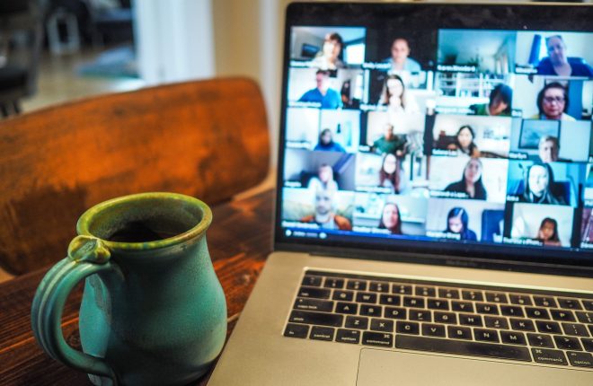 A laptop displaying a grid view of a virtual meeting with multiple participants on screen, alongside a turquoise ceramic mug on a wooden table.